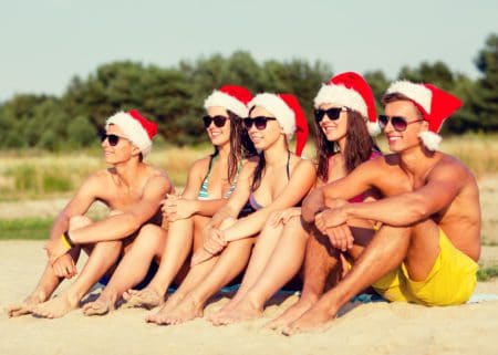 5 people at beach sitting in sand with santa hats on